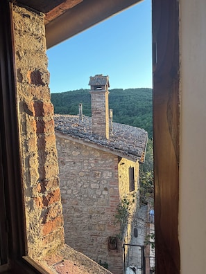 A stone building with a tiled roof and a chimney, viewed through a window with a wooden frame. - A cozy retreat in traditional Tuscan style in the heart of the Siena countryside (Toscana)