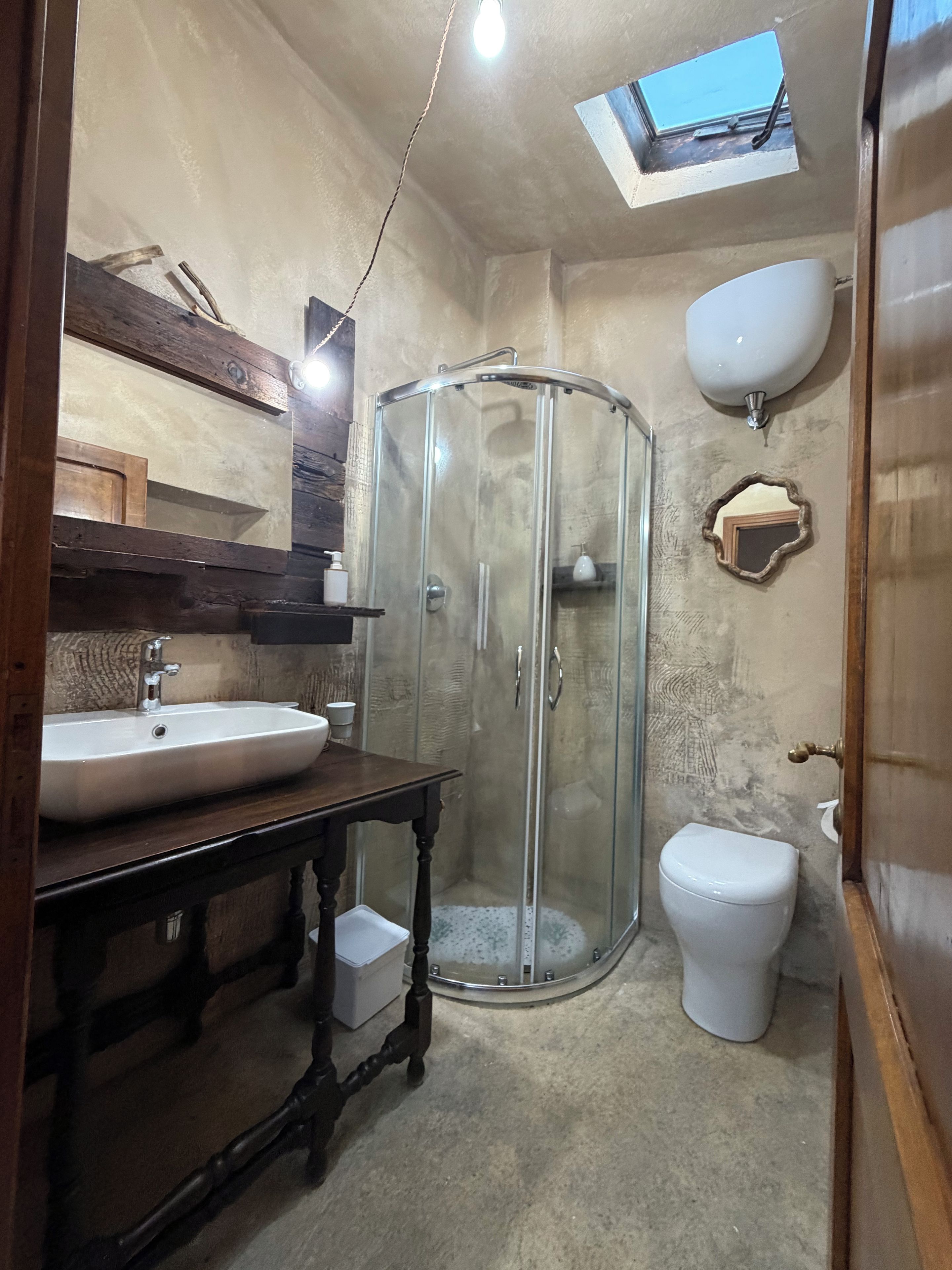Ein Badezimmer mit Duschkabine aus Glas, Waschbecken, Toilette und Dachfenster.
