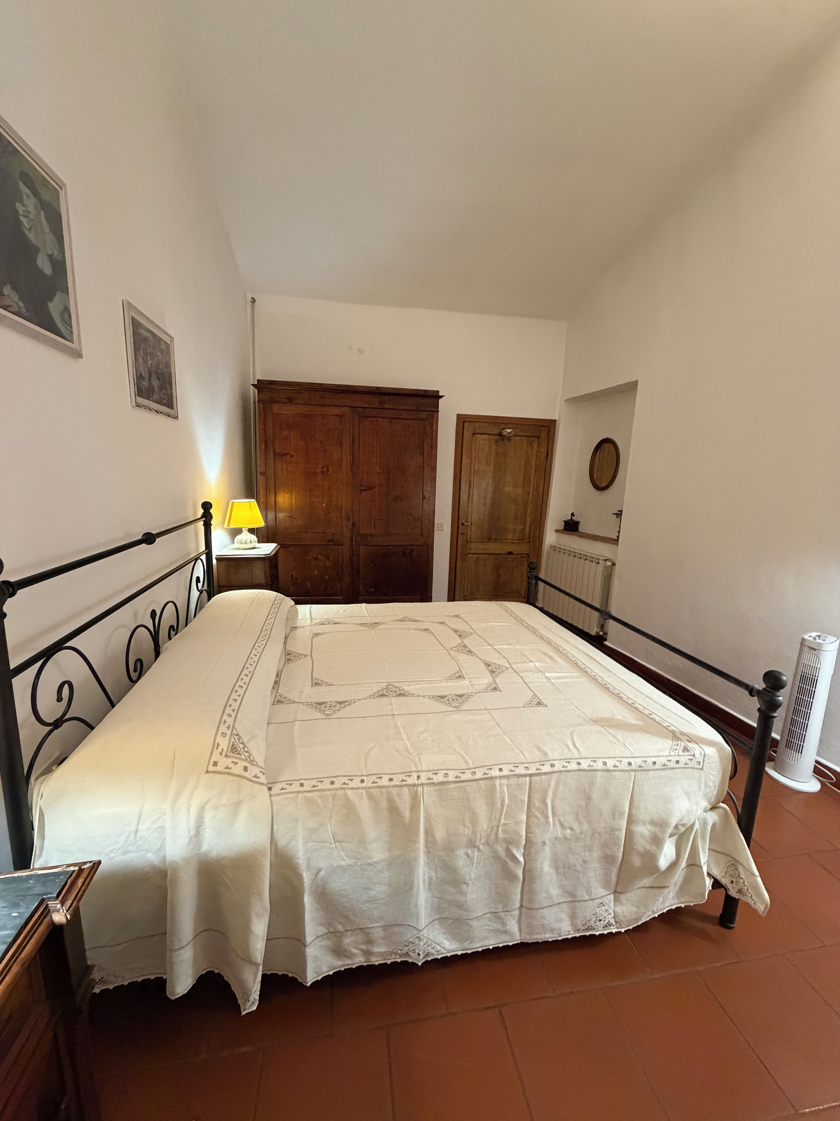 Ein Schlafzimmer mit einem Bett, einem Holzschrank, einer Tür, einem Heizkörper und einer Wandlampe.