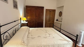 Ein Schlafzimmer mit einem Bett, einem Holzschrank, einer Tür, einem Heizkörper und einer Wandlampe.