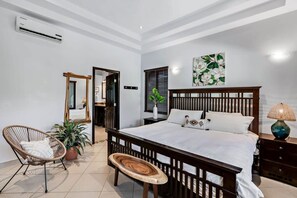 A bedroom with a wooden bed, a chair, a bedside table, and a wall-mounted air conditioner. - Beautiful 4-bedroom house with AC and private pool in Brasilito Beach (Brasilito)