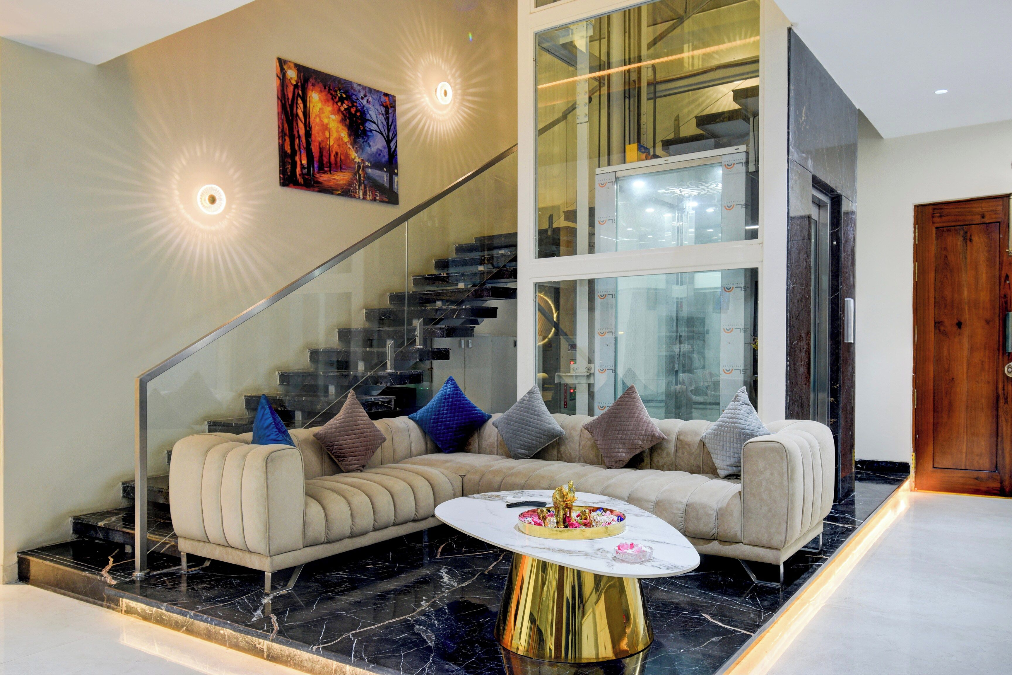 Un salon moderne avec un canapé d’angle, un escalier en verre et un tableau accroché au mur.