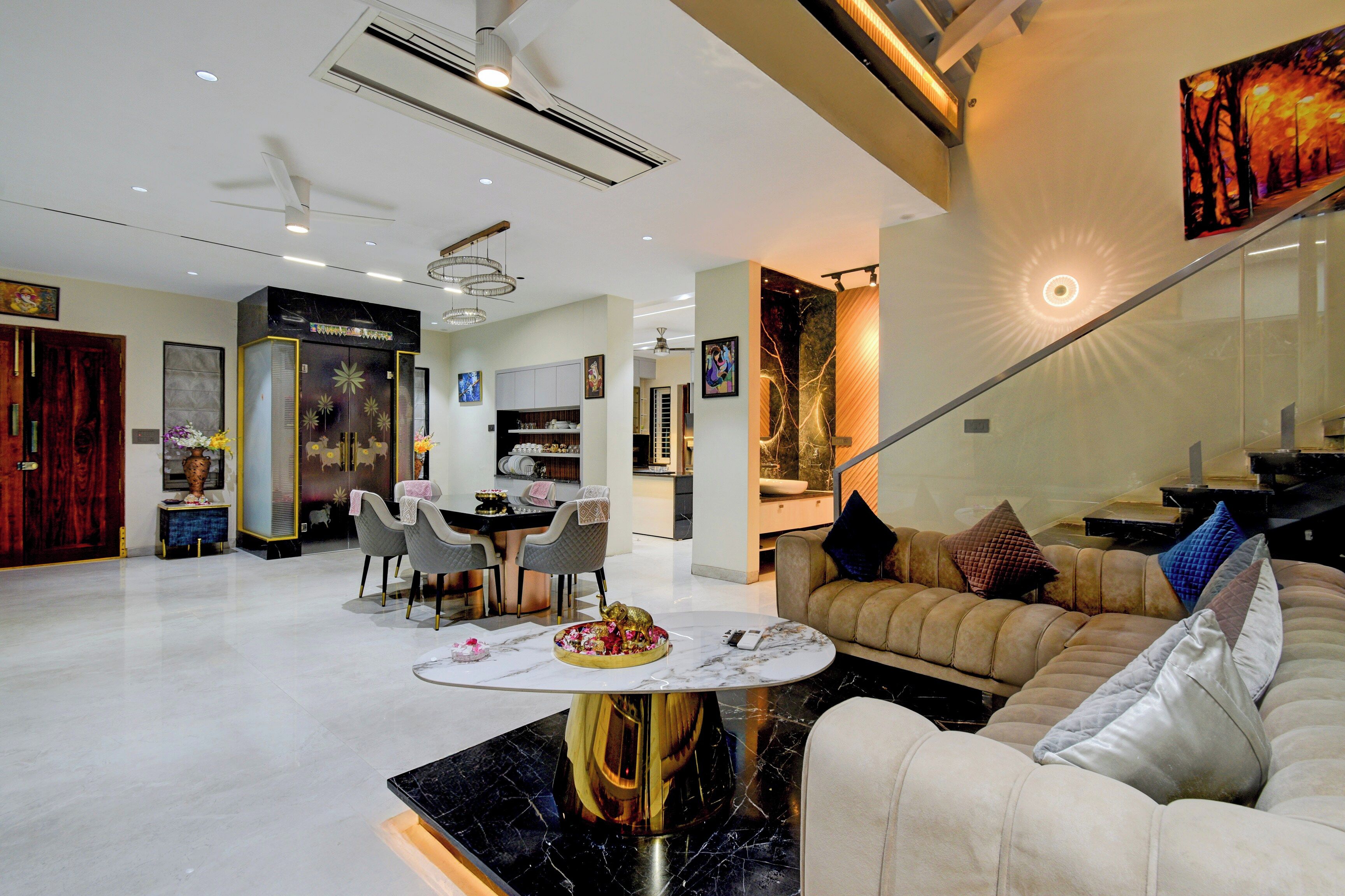 A modern living room with a sofa, a dining area with chairs, a kitchen, and a staircase.