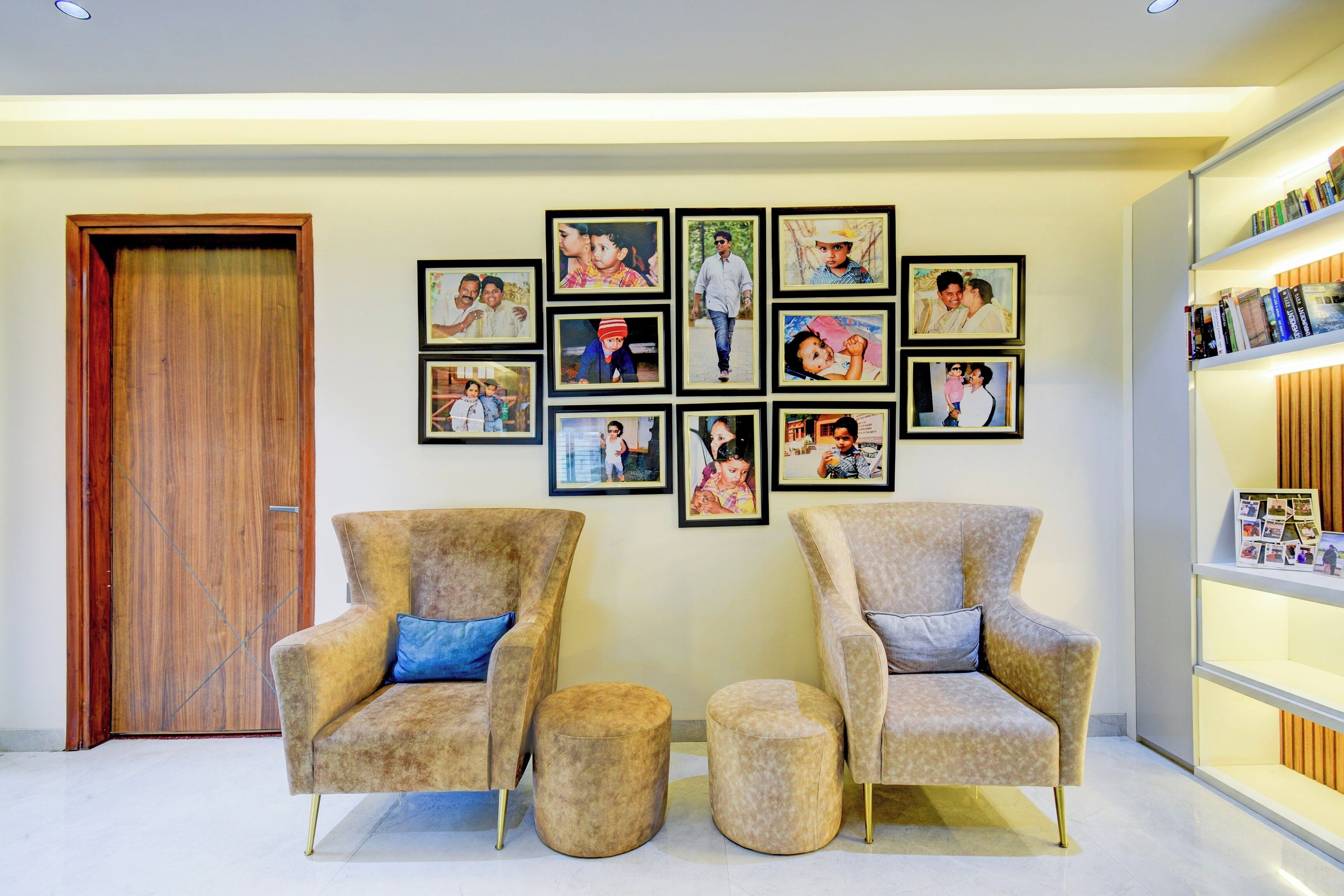 A room with two armchairs, a small ottoman, and a wall adorned with framed photographs.