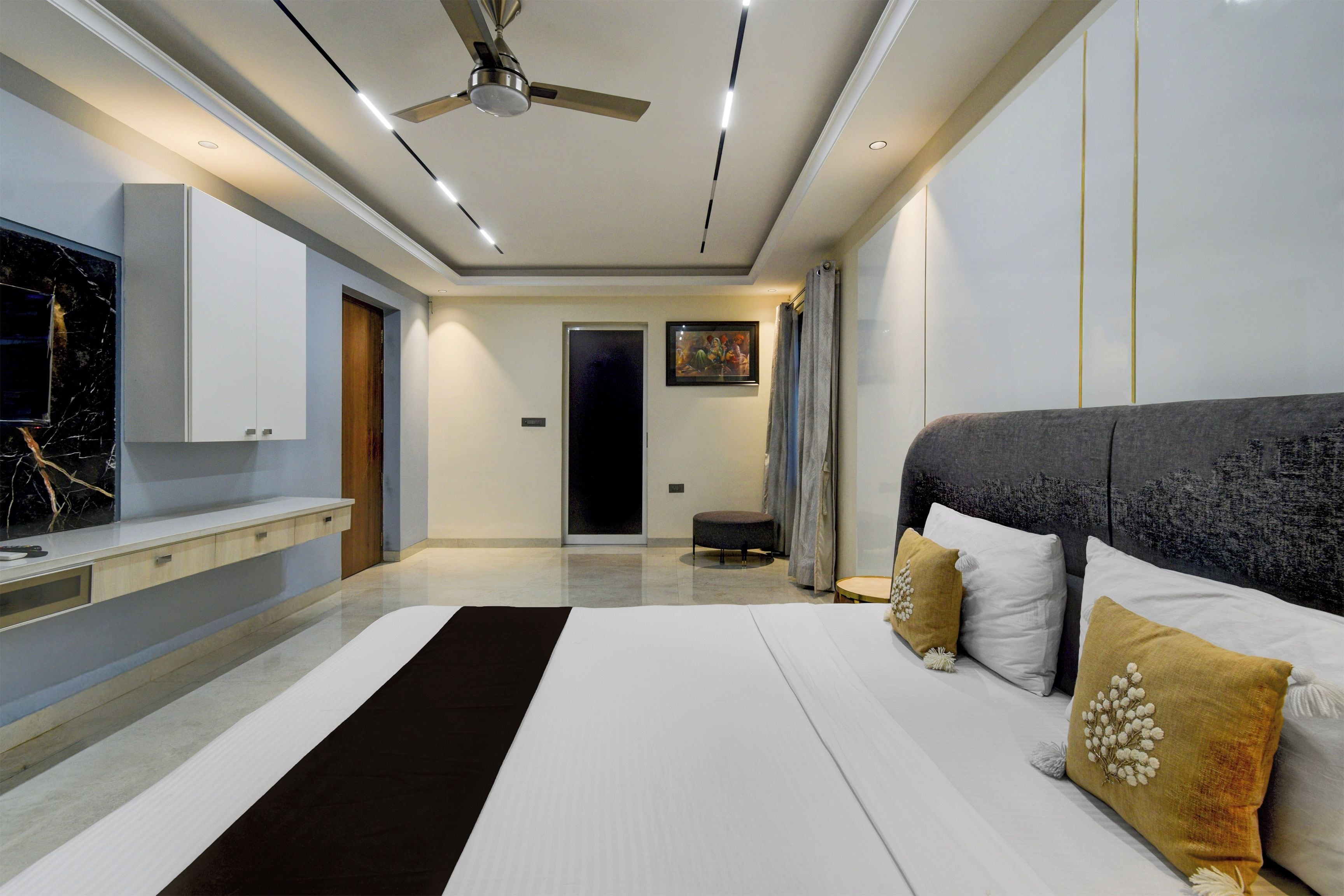 Une chambre à coucher moderne avec un grand lit, un ventilateur de plafond et un téléviseur fixé au mur.