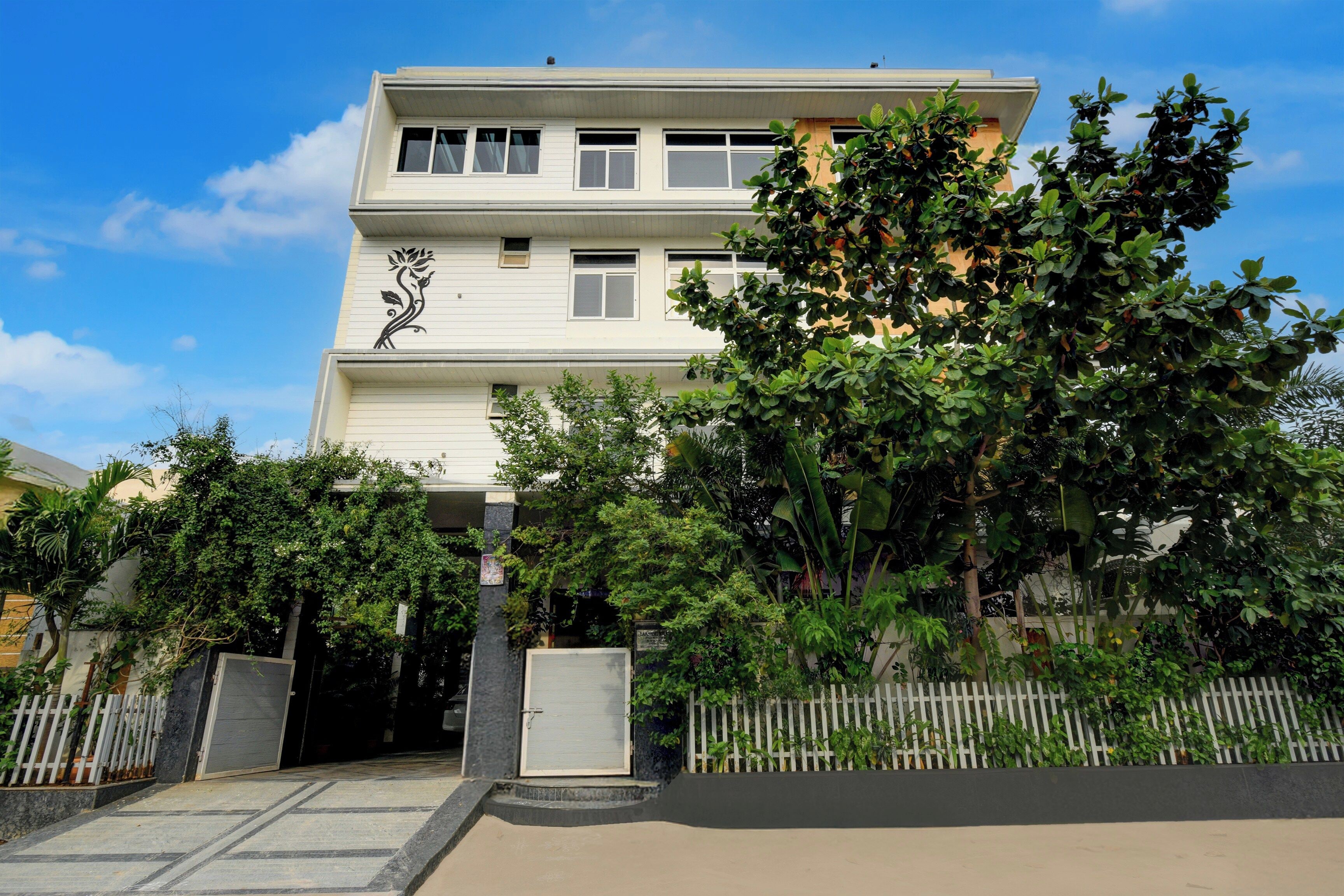 Ein zweistöckiges Gebäude mit weißer Fassade, einem dekorativen schwarzen Blumenmuster im unteren Bereich und einem verschlossenen Eingang mit weißem Zierzaun.