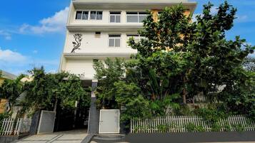 Ein zweistöckiges Gebäude mit weißer Fassade, einem dekorativen schwarzen Blumenmuster im unteren Bereich und einem verschlossenen Eingang mit weißem Zierzaun.