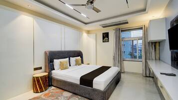 A modern bedroom with a large bed, a ceiling fan, a television, and a window with curtains.