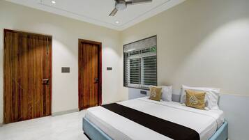 A bedroom with a bed, two wooden doors, a ceiling fan, a window with blinds, and a wall-mounted light fixture.