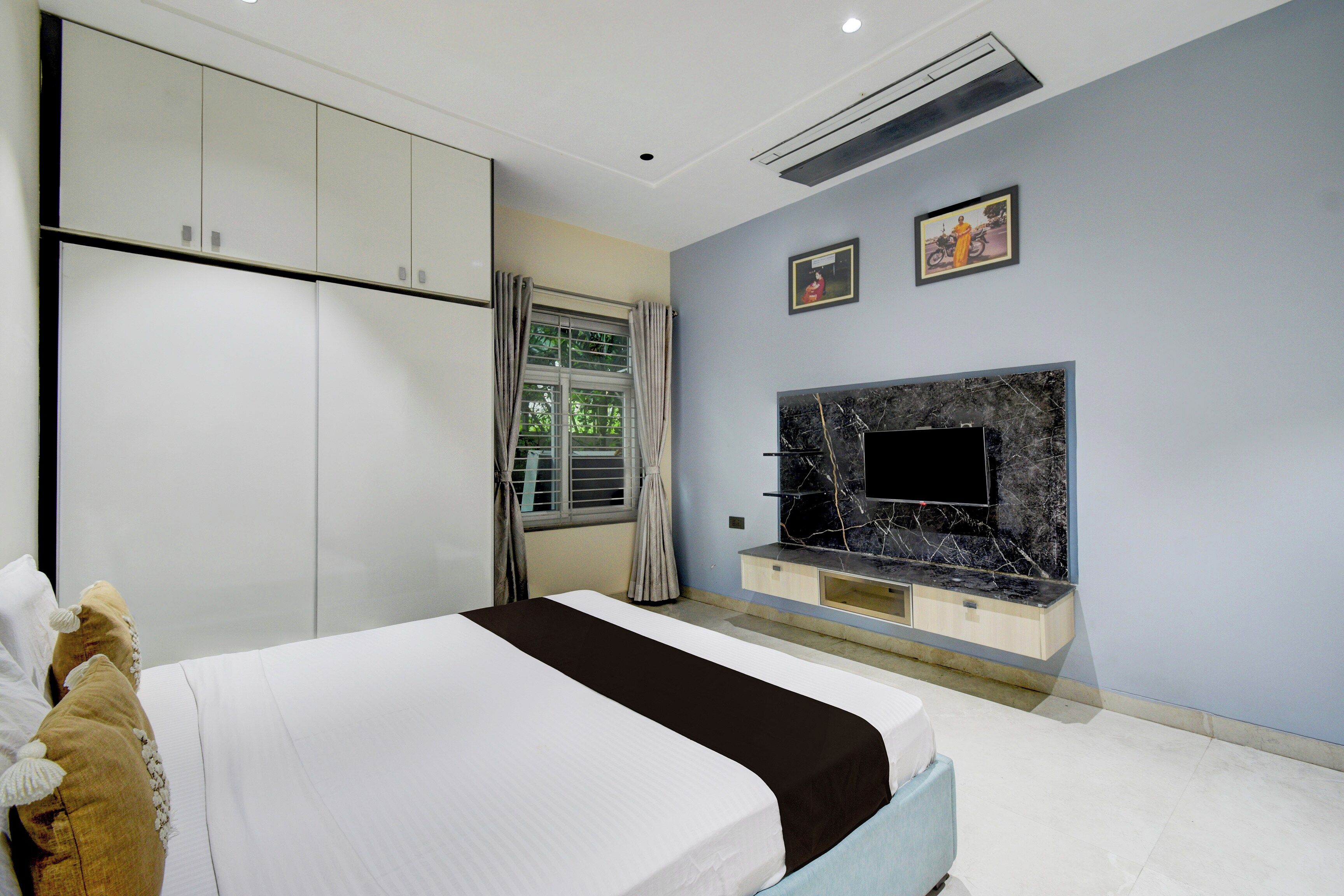 A bedroom with a bed, wardrobe, TV, and artwork on the wall.
