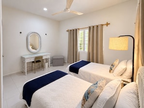 A bedroom with two beds, a vanity with a mirror, a ceiling fan, and a window with curtains. - Mar-e-Luna | Private Pool & Beach Living in Chicxulub (Chicxulub)