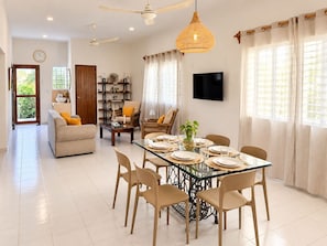 A spacious living area with a sofa, dining table set for four, and a television mounted on the wall. - Mar-e-Luna | Private Pool & Beach Living in Chicxulub (Chicxulub)