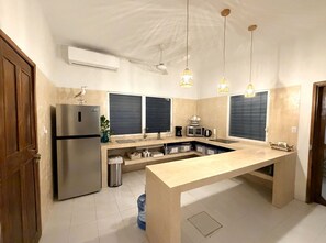 A modern kitchen with a stainless steel refrigerator, a built-in oven, a sink, and a countertop with storage drawers. There are pendant lights above the counter and a ceiling fan. - Mar-e-Luna | Private Pool & Beach Living in Chicxulub (Chicxulub)