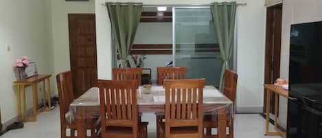 A dining area with a table and chairs, a refrigerator, a ceiling fan, and a window with curtains.
