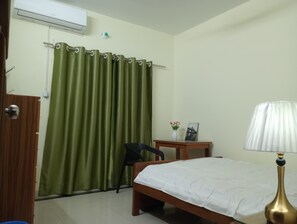 A hotel room with a bed, a chair, a small table with a vase of flowers, and a lamp.