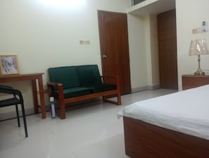Ein Zimmer mit einem Bett, einem grünen Sofa, einem Holztisch und einem Stuhl.