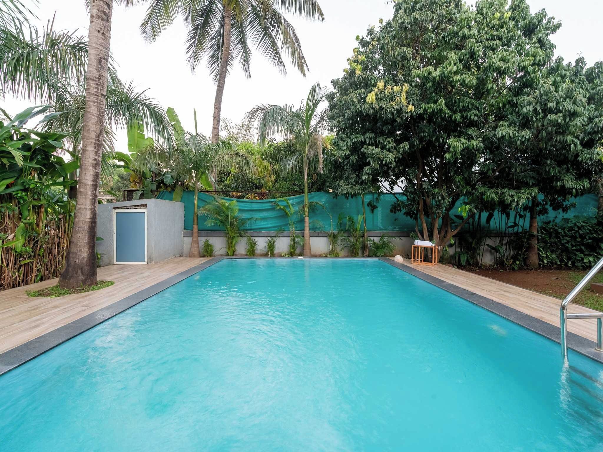 Una piscina rectangular con un deck de madera alrededor, bordeada por un muro bajo y una valla verde.