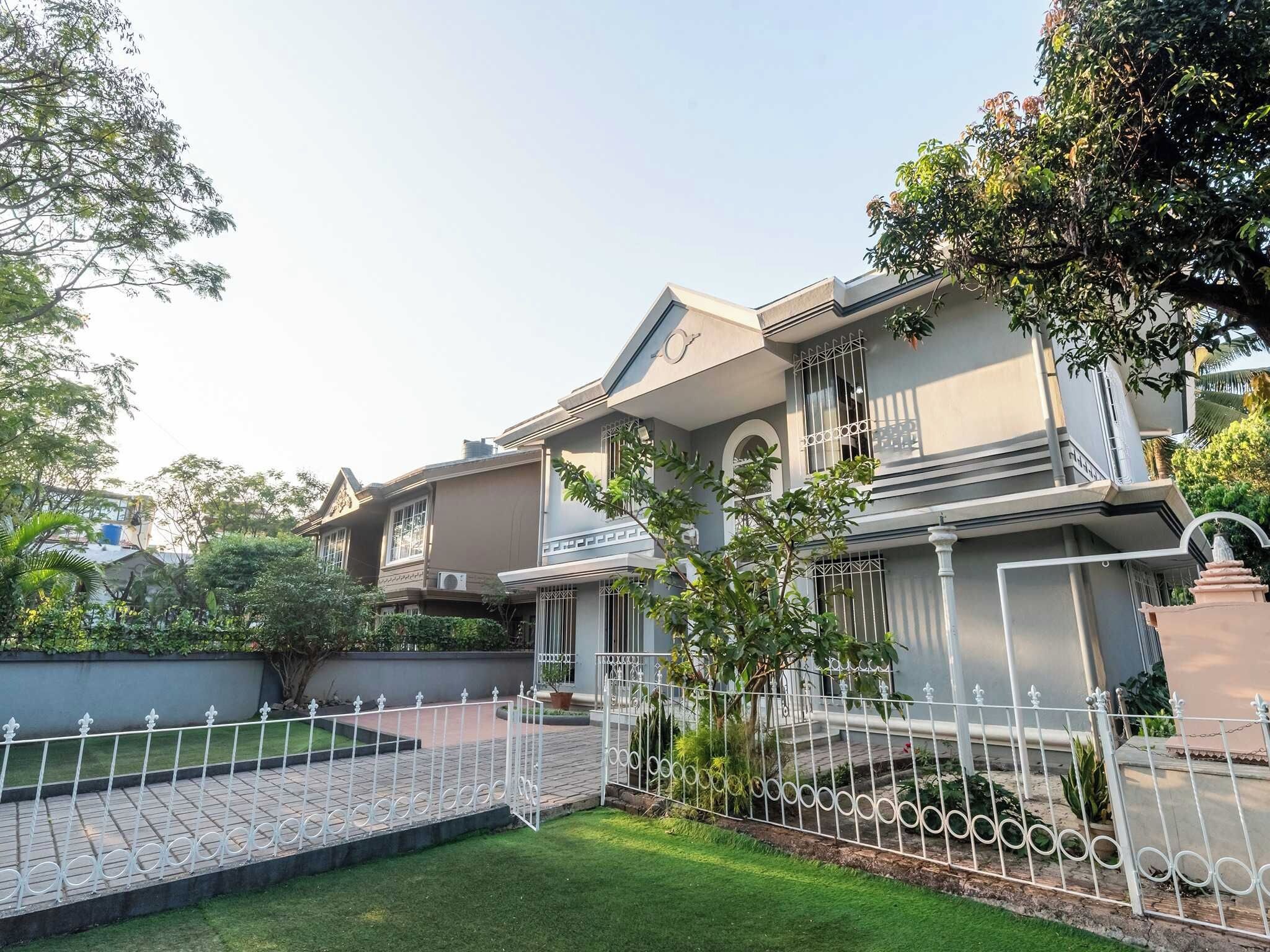 A two-story house with a balcony, a fenced garden, and a clear sky.