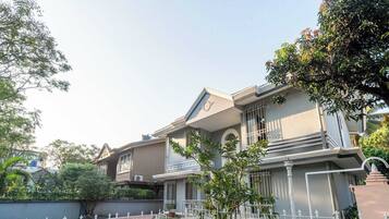 A two-story house with a balcony, a fenced garden, and a clear sky.