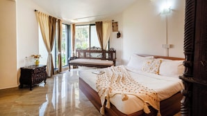 Quarto com uma cama grande, um banco de madeira, uma mesa de cabeceira e uma janela com cortinas.