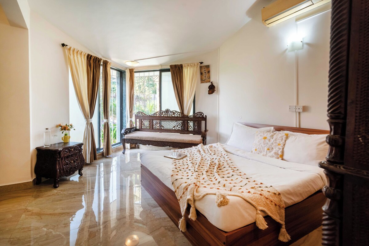 A bedroom with a large bed, a wooden bench, a nightstand, and a window with curtains.