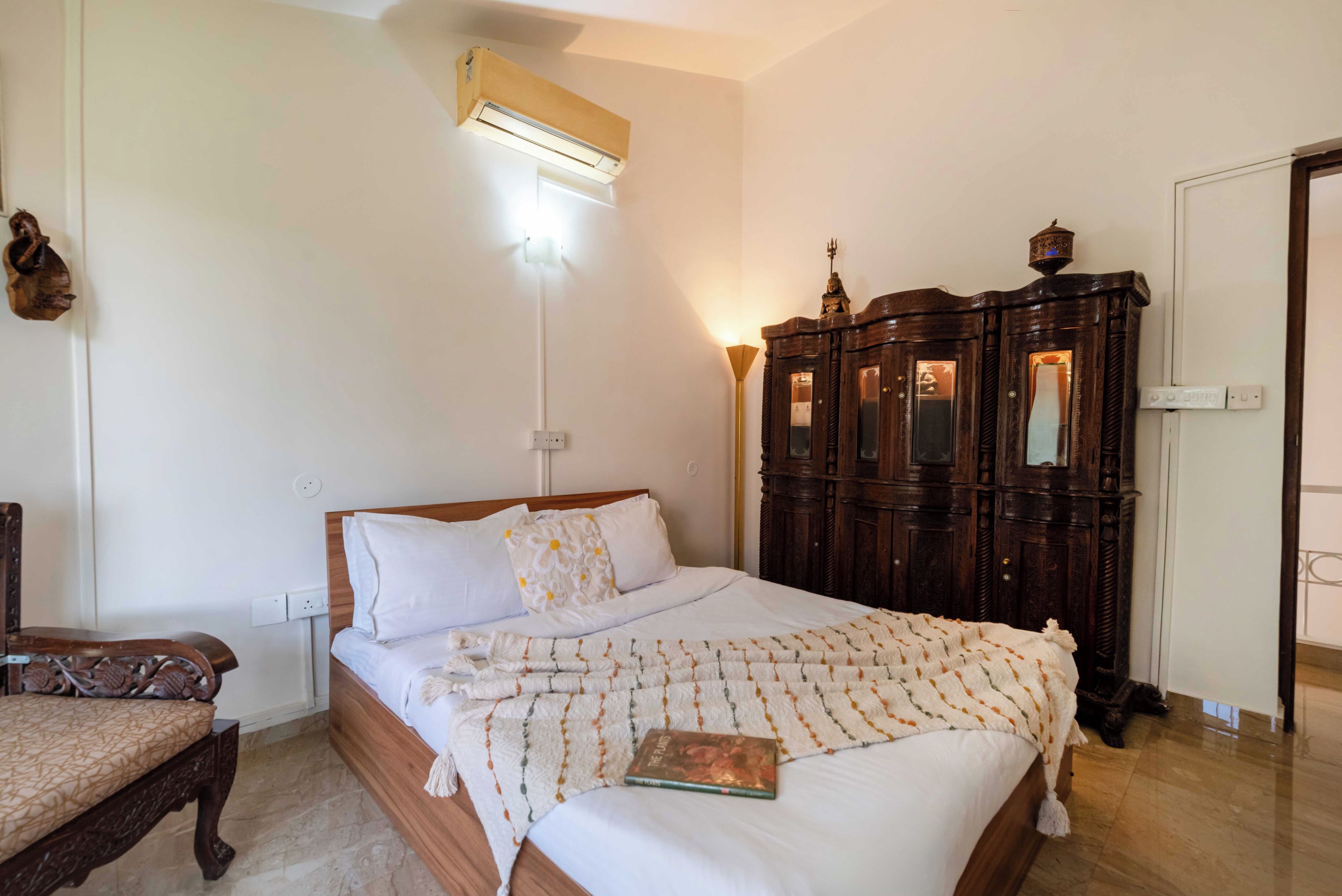 Un dormitorio con una cama, un armario de madera, una mesita de noche y un aire acondicionado de pared.