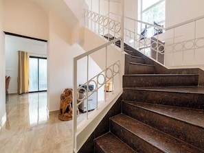 Un escalier avec une rampe en métal, une statue et un appareil Tuffon, le tout dans une pièce bien éclairée grâce à une grande fenêtre.