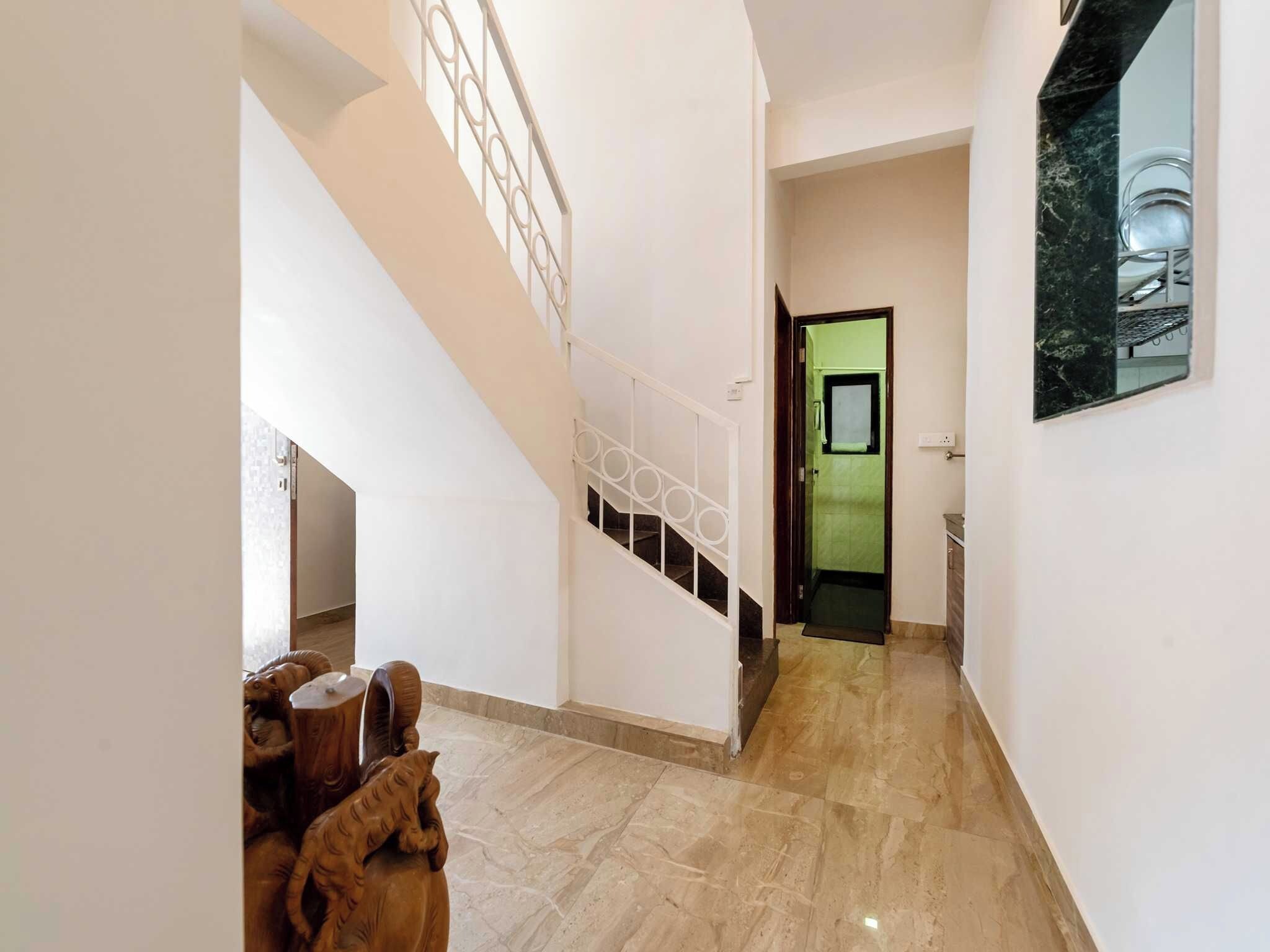 Um corredor com escada, área de jantar com mobiliário de madeira e uma porta verde que dá para outro cômodo.