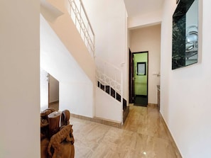A hallway with a staircase, a dining area with wooden furniture, and a green door leading to another room. - DanCenter Trizi Villa 4BHK with Pvt Pool (Lonavala)