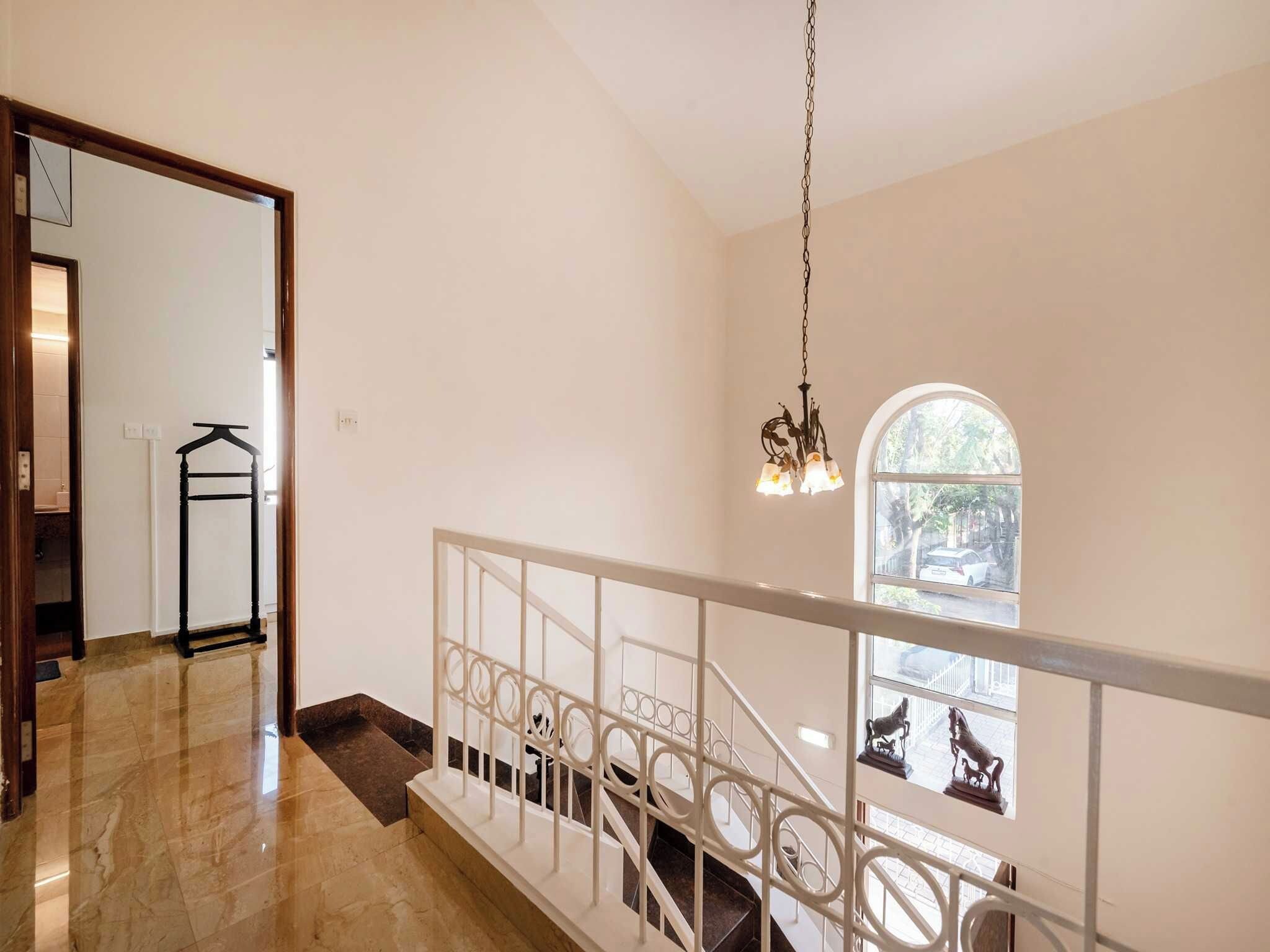 A staircase with white railings and a chandelier, leading to a landing with a view of the street.