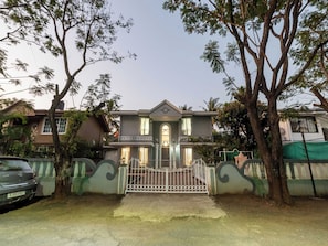 A two-story house with a gated entrance, surrounded by trees and a parked car. - DanCenter Trizi Villa 4BHK with Pvt Pool (Lonavala)