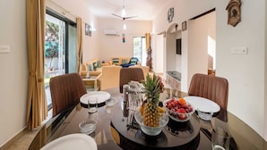 Uma sala de jantar com mesa redonda, cadeiras e uma cesta de frutas.