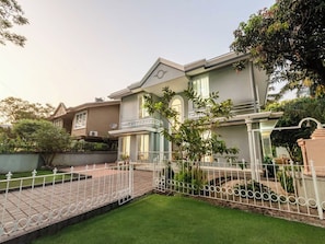 Une maison à deux étages avec un jardin devant, une clôture blanche et une allée pavée.