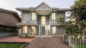 Uma casa de dois andares com fachada simétrica, uma entrada central com arco decorativo e um caminho de paralelepípedos que leva à porta da frente.