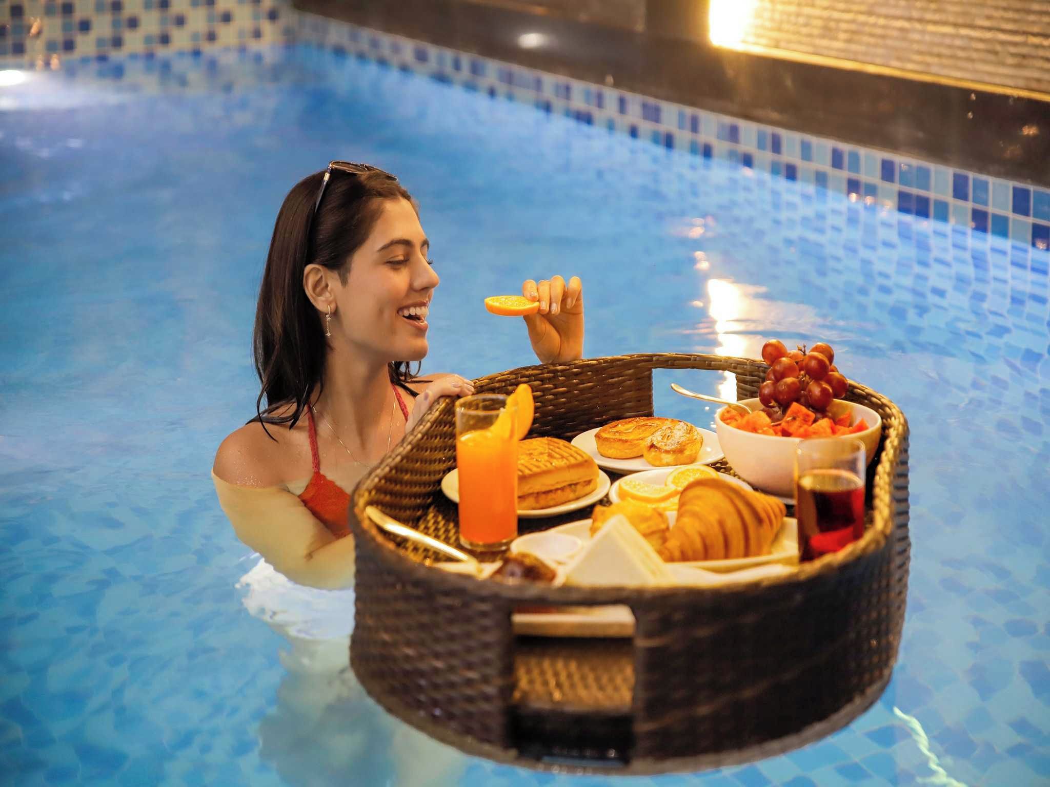 Una persona en una piscina sosteniendo una bandeja con comida y bebidas.