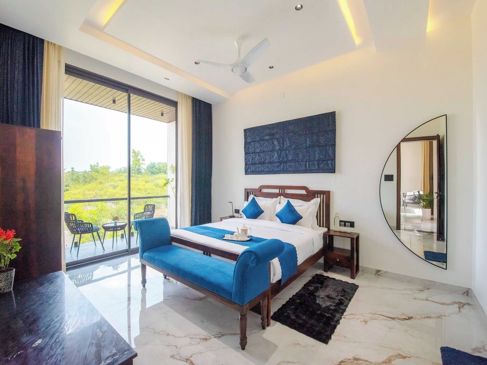 A modern hotel room with a large bed, a balcony, and a view of greenery.
