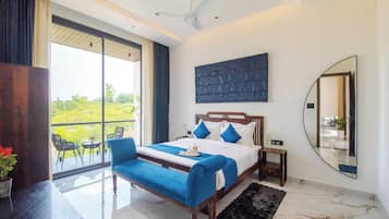 A modern hotel room with a large bed, a balcony, and a view of greenery.