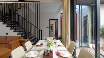 A dining area with a long table set for six, a sofa, and a staircase.