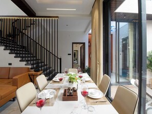 Espaço de refeições com uma mesa comprida posta para seis pessoas, um sofá e uma escada.