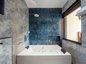 A modern bathroom with a large bathtub, dark marble walls, and a window providing natural light. - DanCenter Papillon Villa 5BHK with Pool (Udaipur)
