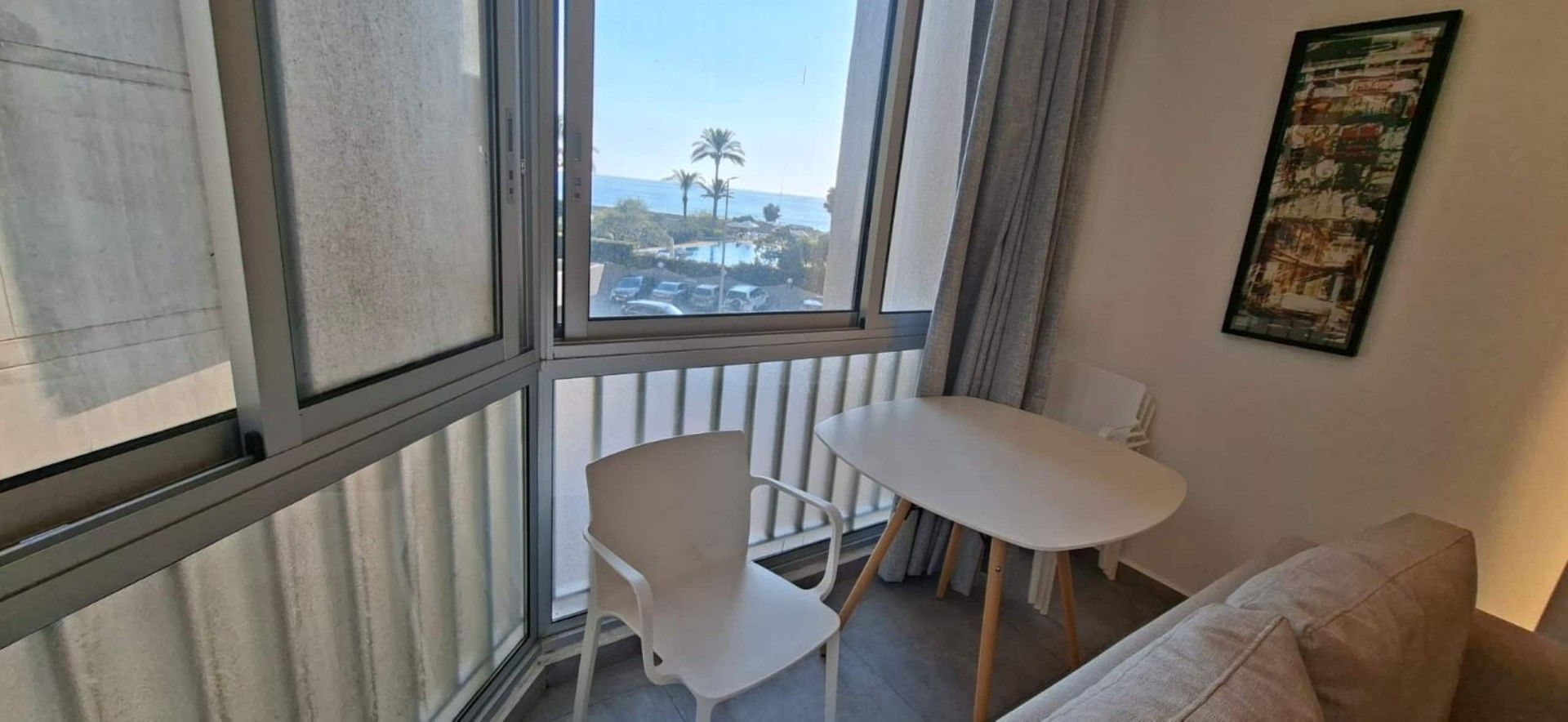 A room with a white chair, a small white table, and a view of the sea through a window.