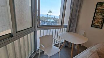 A room with a white chair, a small white table, and a view of the sea through a window.
