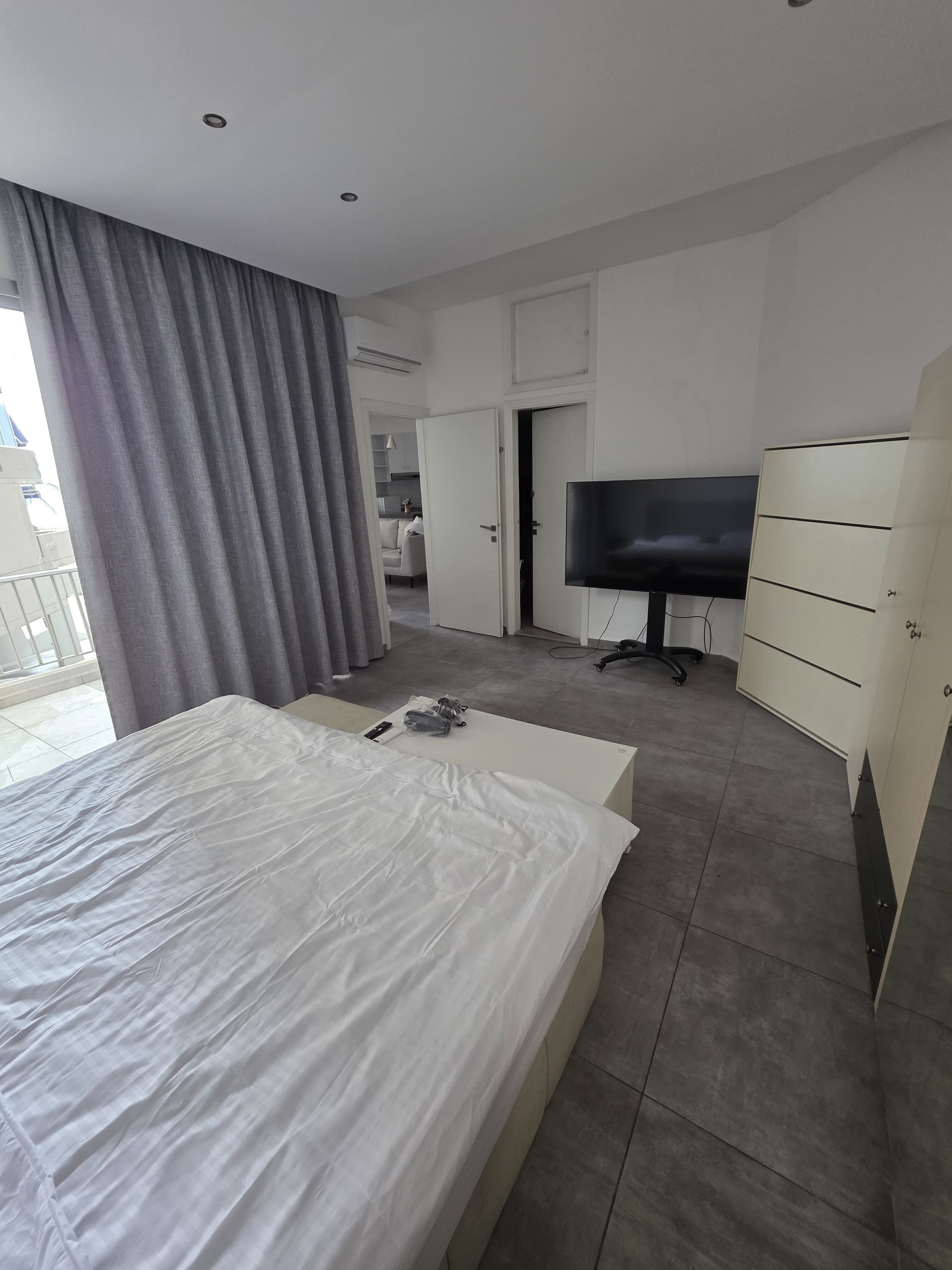 A modern hotel room with a large bed, a television, a wardrobe, and a bathroom visible through an open door.