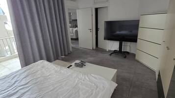 A modern hotel room with a large bed, a television, a wardrobe, and a bathroom visible through an open door.