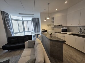 Eine moderne Küche mit weißen Schränken, einer zentralen Kochinsel und einem Essbereich mit einer Couch und Stühlen.