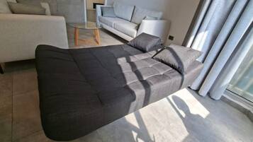 A modern living room with a dark sofa, a glass coffee table, and a light-colored sofa in the background.