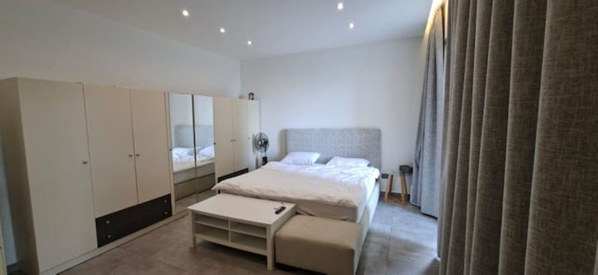 A modern bedroom with a bed, a wardrobe, a bedside table, and a mirror.