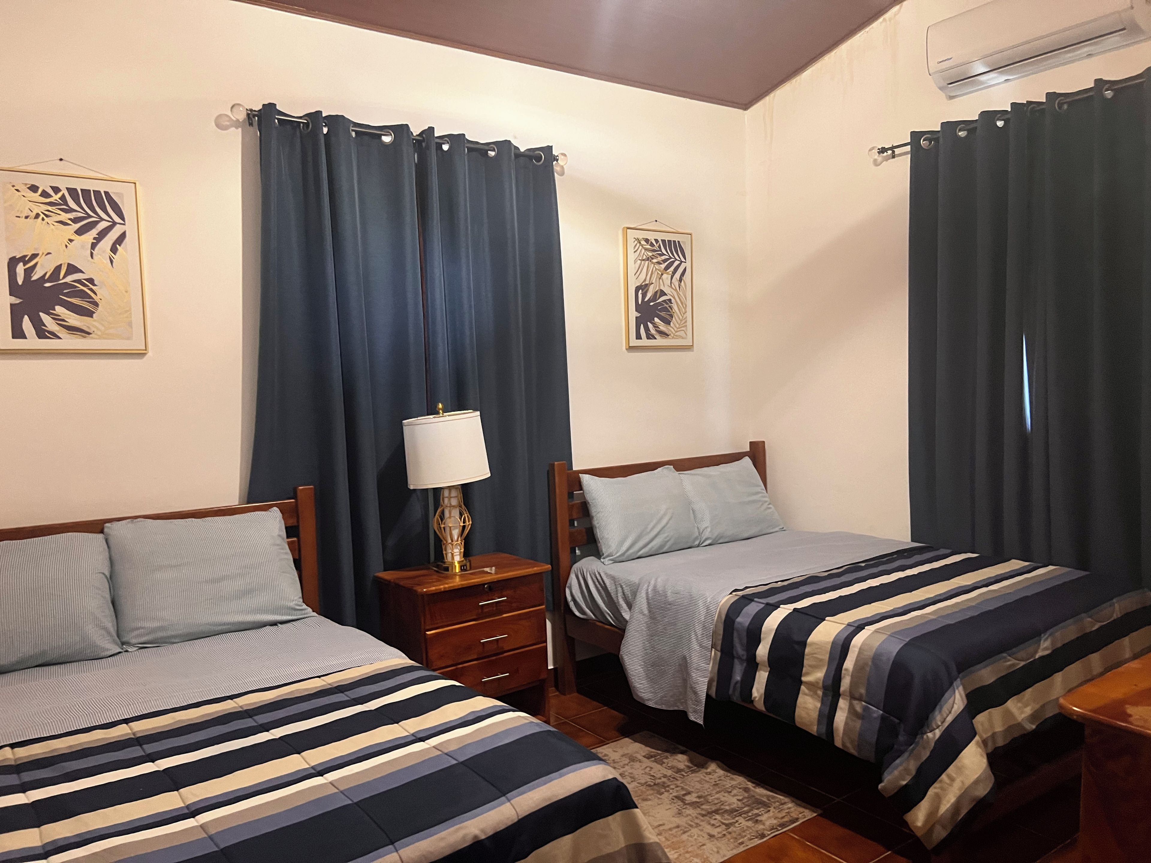 Ein Zimmer mit zwei Betten, einem Nachttisch, einer Lampe und Vorhängen.