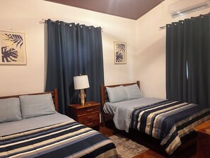 Ein Zimmer mit zwei Betten, einem Nachttisch, einer Lampe und Vorhängen.