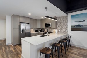 A modern kitchen with a central island, stainless steel appliances, and a bar seating area. - Porsche Suite (Buffalo)